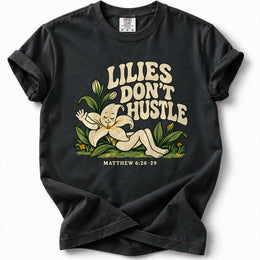 Lilies Don’t Hustle Premium T-Shirt in Black, front view with botanical character inspired by Matthew 6:28–29